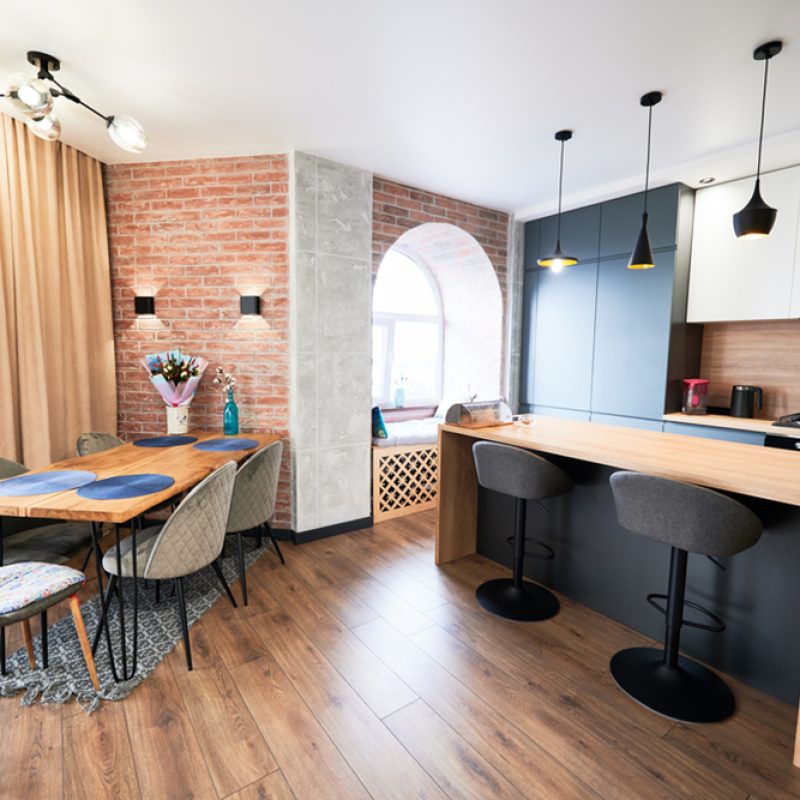 Living room and kitchen studio in dark blue color with modern furniture table, chair and stylish lamps. Concept of stylish modern interior kitchen with bar table.